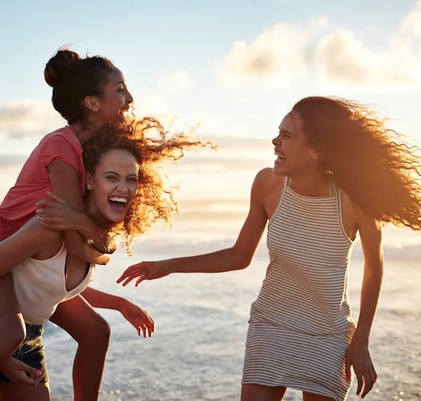 Three young women laughing joyfully on a sunny beach, capturing the essence of a memorable trip with friends.