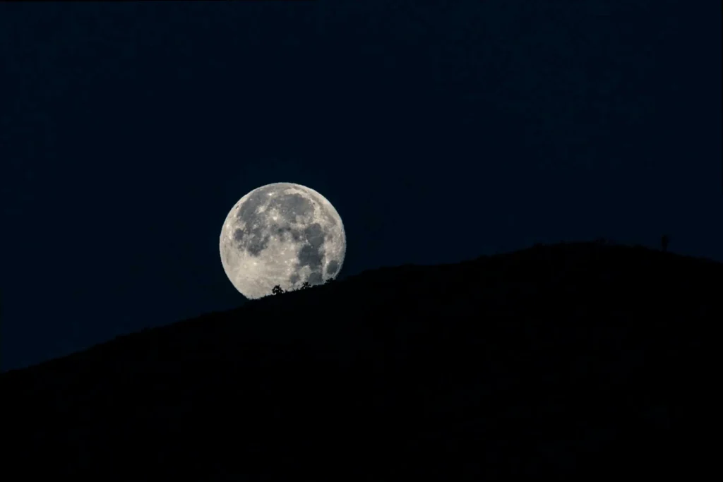 A full moon shining over a distant landscape, representing good night wishes across miles