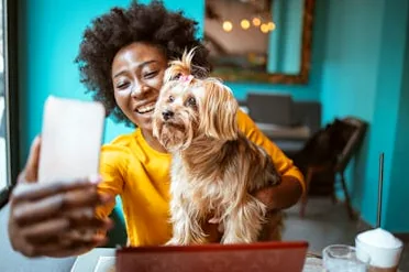 A woman laughing and playing with her dog, embodying the joyful and sometimes chaotic reality of pet parenthood.
