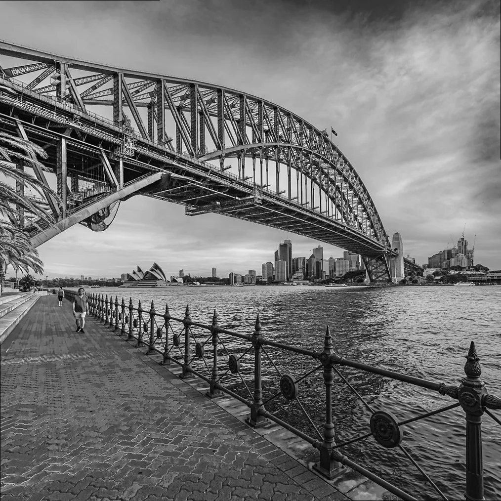 Iconic Sydney Harbour Bridge in black and white, showcasing dramatic architectural contrast and timeless design against a textured sky.