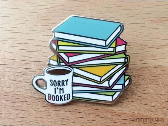 a close-up of an enamel pin that says 'sorry i'm booked' on a pink background, ideal for bookish humor and social media.