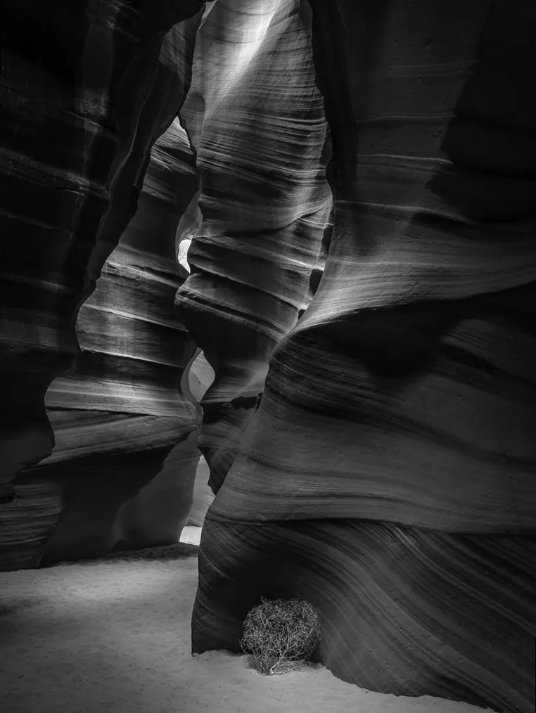 Dramatic black and white landscape of Antelope Canyon, with light filtering through narrow rock formations, creating strong contrasts and sculpted shadows.
