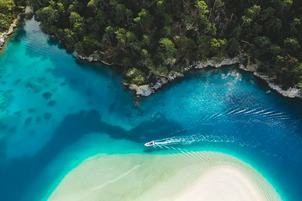 Aerial view of a serene blue lagoon with turquoise sea, white sand beach, and a tourist boat, representing an idealized nature escape