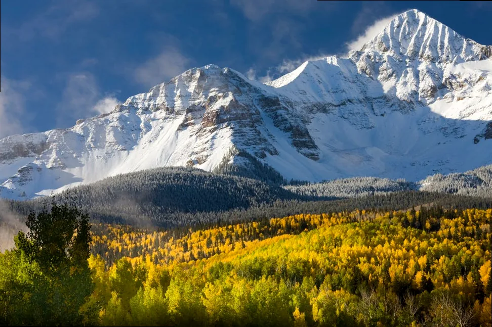 Scenic snow-capped mountain vista with aspen trees in autumn colors, inspiring captions about grand landscapes or seasons.