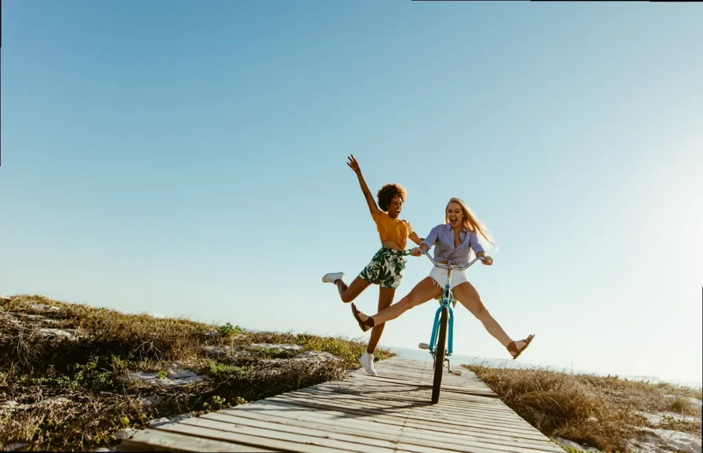 Group of excited young women laughing and having fun while riding bikes and running on a boardwalk, embodying joy and humor in everyday life.