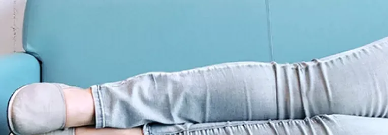 Person lounging with legs stretched out on a blue sofa, laptop nearby, symbolizing relaxed productivity and work-life flexibility.