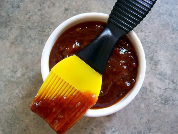 A vibrant BBQ sauce being brushed onto sizzling ribs, showcasing rich flavor and a glossy texture.