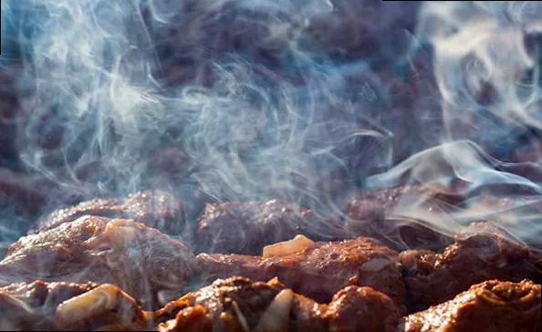 Thick, aromatic smoke rising from a traditional offset smoker, enveloping cuts of meat on the grates.