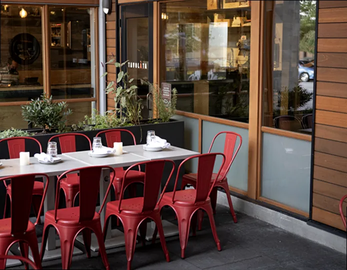 A happy dog sitting patiently at a table on a vibrant restaurant patio, looking at a bowl, ready to enjoy a pet-friendly meal.