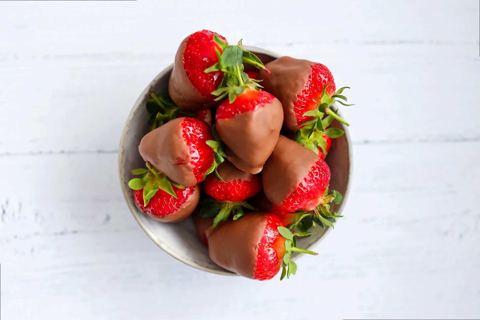 A close-up image of glistening chocolate-covered strawberries, some with white chocolate drizzle, artfully arranged on a platter, evoking romance and indulgence.