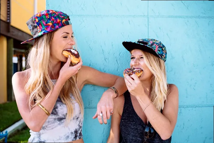 Two hands reaching for a box of colorful, frosted donuts, symbolizing shared sweet moments and affection.