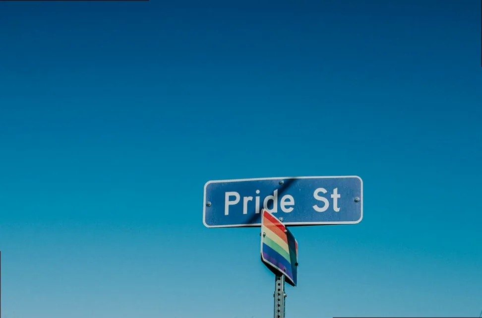 American road sign for 'Pride Street' with a rainbow flag, symbolizing funny Pride Month captions.