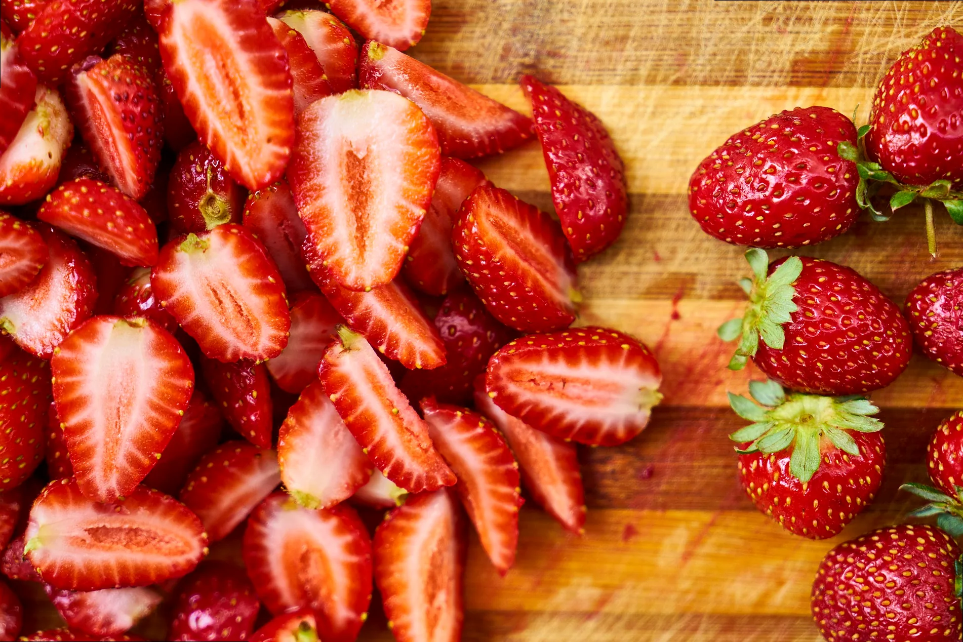 Close-up of hands, some stained with red, carefully picking ripe, red strawberries from green plants in a sunlit field, emphasizing the hands-on, slightly messy fun of strawberry picking.