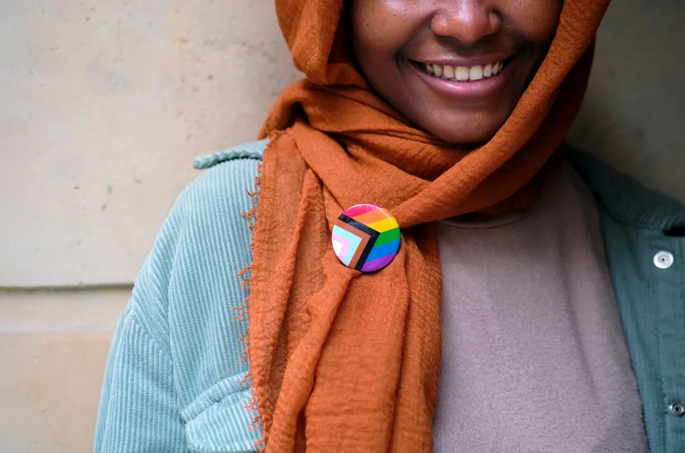 Smiling Muslim woman with an LGBTQ pride pin, celebrating inclusive pride month.