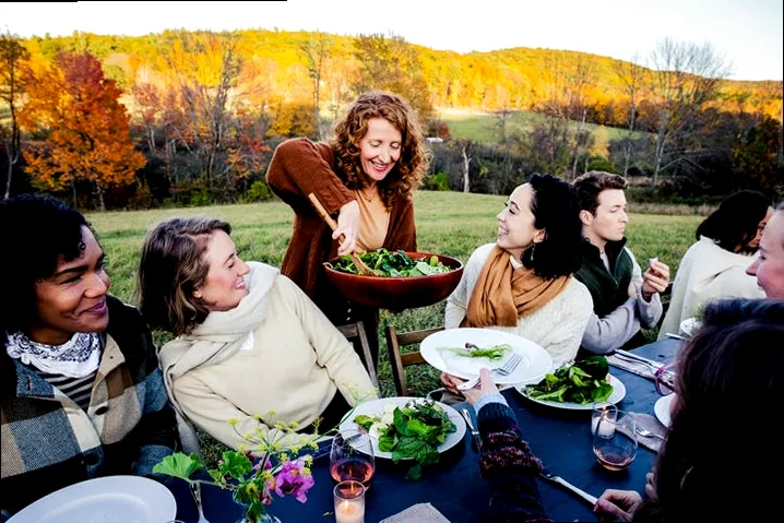 Friends gathered happily around a table, sharing food and laughter at a Friendsgiving dinner.
